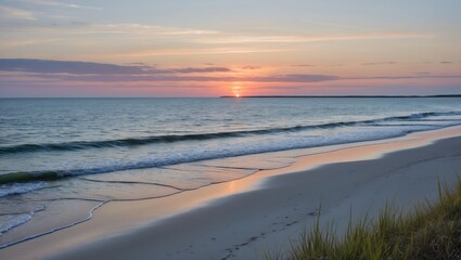 Sunset over calm ocean waves with sandy beach and grass in foreground against colorful sky in coastal landscape scene