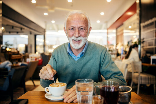 Portrait of senior man stirring coffee in coffee shop and smiling at camera.