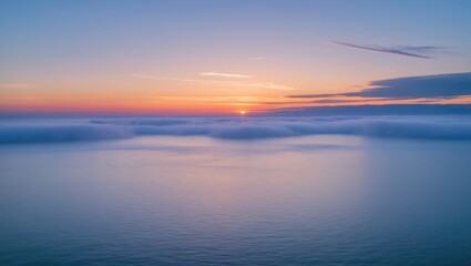 Obraz premium Sunset over calm ocean with gentle waves and fog covering the water illuminated by warm colors in the sky.