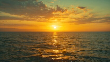Obraz premium Sunset over calm ocean waters with reflection on the surface and clouds in the sky creating a gradient of warm colors.