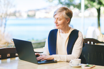 Outdoor portrait of mature 55 - 60 year old woman working with laptop