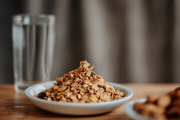 A healthy breakfast scene with granola in a white plate, a glass of water, and a wooden table, perfect for promoting nutrition, wellness, and morning routines.