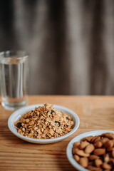 A healthy breakfast scene with granola in a white plate, a glass of water, and a wooden table, perfect for promoting nutrition, wellness, and morning routines.