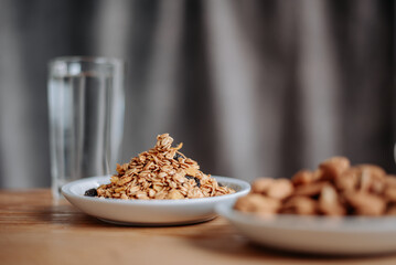 A healthy breakfast scene with granola in a white plate, a glass of water, and a wooden table, perfect for promoting nutrition, wellness, and morning routines.