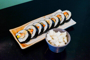 Kimbap on white plate and radish,Gimbap is Korean seaweed rice roll filled with a variety of delicious fillings, egg, carrot, ham, tuna,gochujang sauce,served with kimchi, The street food of Korea..