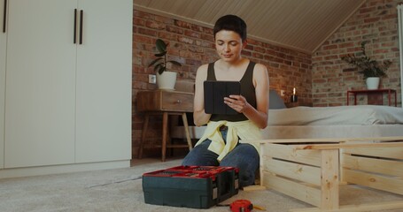 A woman selects tools from a toolbox by assembling a rack while sitting on the floor at home