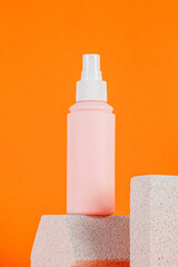 Cosmetic pink bottle. Womens cosmetic accessory for makeup with stylish props on orange background.