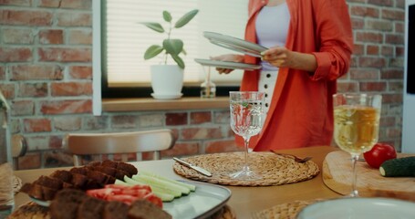 A woman puts plates on the table, setting the table for dinner at home. Close-up of a woman's hands, no face