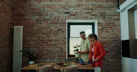 Fototapeta premium Husband and wife are getting ready for dinner. A man sets the table, a woman cuts vegetables in a stylish home kitchen