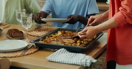A woman puts fried potatoes on the plates of her friends during a joint dinner at home