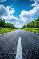 Fototapeta premium Serene asphalt road stretches through lush green forest under a bright blue sky with fluffy white clouds scenic journey