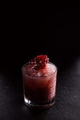 Red cocktail with ice in an old fashioned glass. A piece of pomegranate decorates the refreshing drink. Long alcoholic drink for a bar cocktail card. Party concept for girls.