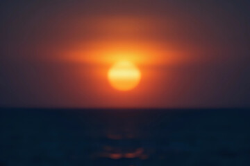 Out of focus sun setting over the ocean glowing orange with dark blue background.
