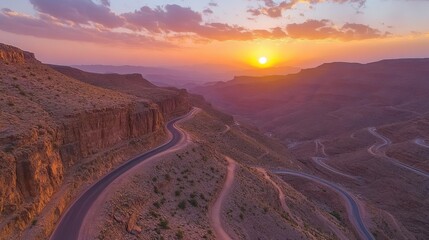 Serpentine Road Winding Through Majestic Mountain Landscape at Sunset Breathtaking Aerial View of Rugged Terrain and Dramatic Sky Golden Hour Light