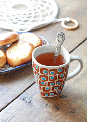 Ceramic mug with a brown ornament with tea on the wooden kitchen table with a plate of pastries. Selective focus on the mug.