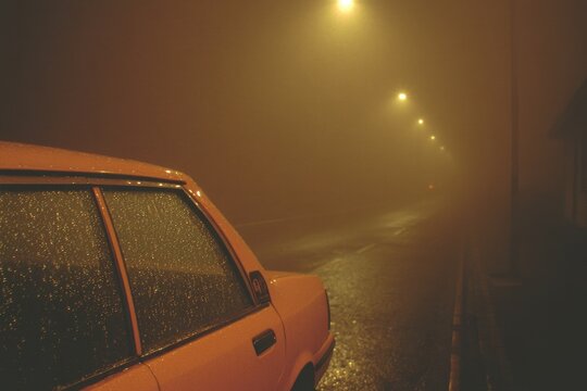 Foggy night scene with an orange car parked under dim streetligh