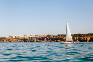 Sailboat Near Coastal Town with Cliffs and Clear Blue Sky