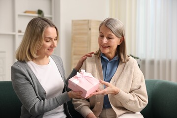 Smiling daughter congratulating her mom with gift on sofa at home. Happy Mother's Day