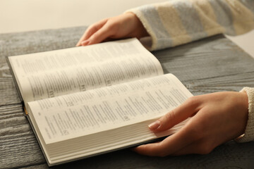 Woman with open Holy Bible in English language at wooden table, closeup
