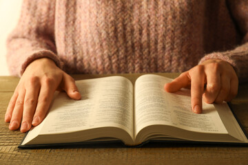 Woman reading Holy Bible in English language at wooden table, closeup