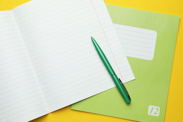 Copybooks and pen on yellow background, top view