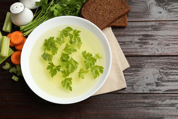 Tasty chicken bouillon in bowl with bread and ingredients on wooden table, flat lay. Space for text