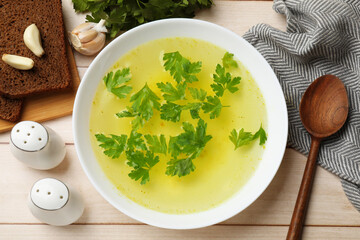 Tasty chicken bouillon in bowl served on wooden table, flat lay
