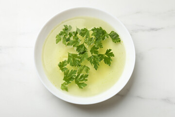 Tasty chicken bouillon in bowl on white marble table, top view