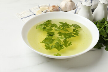 Tasty chicken bouillon in bowl and ingredients on white marble table, closeup