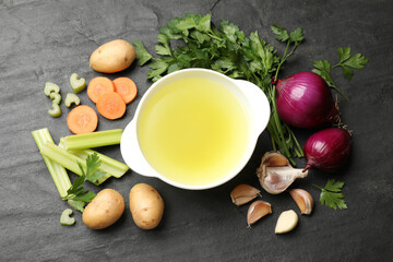 Tasty chicken bouillon in bowl and ingredients on black table, flat lay