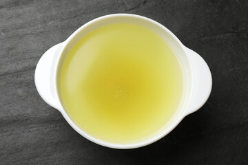 Tasty chicken bouillon in bowl on black table, top view
