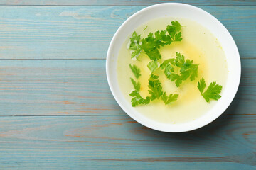 Tasty chicken bouillon with parsley in bowl on light blue wooden table, top view. Space for text