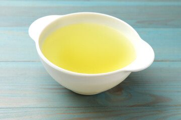 Tasty chicken bouillon in bowl on light blue wooden table, closeup
