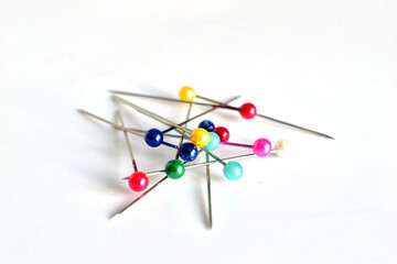 Sewing pins with colored heads lie on a white background.