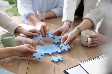 Unity concept. People putting puzzle pieces together at wooden table indoors, closeup