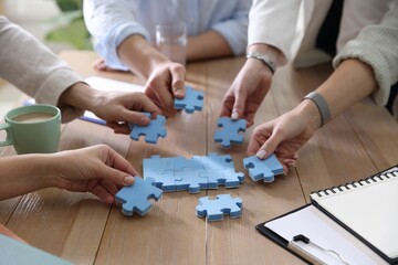 Fototapeta premium Unity concept. People putting puzzle pieces together at wooden table indoors, closeup