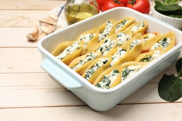 Delicious pasta with ricotta cheese and spinach in baking dish on wooden table, closeup