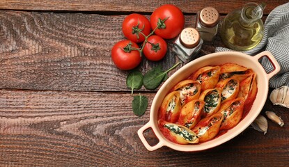Delicious conchiglie pasta with ricotta cheese, spinach and tomato sauce in baking dish on wooden table, flat lay. Space for text