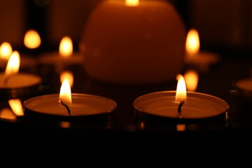 Many burning candles on dark surface, closeup