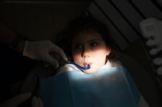 Young girl receiving dental treatment with a saliva ejector in a dimly lit clinic