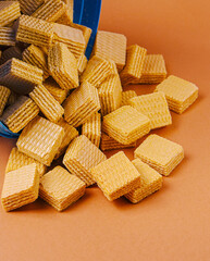 Sweet wafers spilled out of a blue container on orange surface