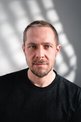 Fototapeta premium Intensives Porträt eines Mannes mit Bart und schwarzem Shirt im Schattenspiel