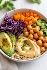 A colorful quinoa bowl features chickpeas, avocado, purple cabbage, cucumbers, and diced carrots topped with a creamy dressing, set in a vibrant kitchen