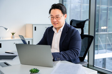 Confident male professional using a laptop, adorned in formal attire, set in a contemporary corporate office with natural lighting and sleek furnishings, conveying productivity and success.