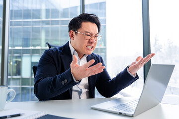 Professional businessman visibly frustrated with computer issues at a modern office. Wearing formal attire and engaged in distressful gesturing. Captures the stress and challenges of corporate life.