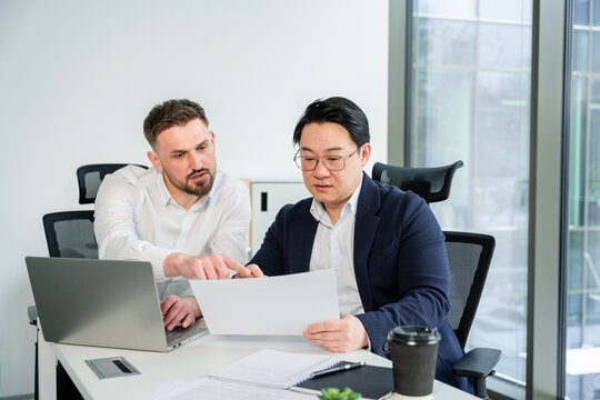 Coworkers analyzing a document together at a modern workplace, fostering teamwork and professional collaboration. Focused atmosphere, business attire adds to the sense of refined professionalism.