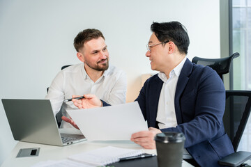 Fototapeta premium Confident professionals engaged in a business meeting in a modern office, discussing work strategies. A formal atmosphere with laptop and documents represents teamwork and productivity.