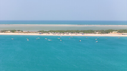 Aerial view of Dhanushkodi’s famous road cutting through the Indian Ocean, with fishing boats scattered along the coastline. with small houses