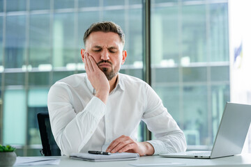 Professional businessman experiencing pain at a modern office desk, portraying discomfort and...