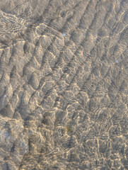 Natural rippled sand texture under clear shallow water with sunlight reflections. Perfect as a background, texture, or overlay for design